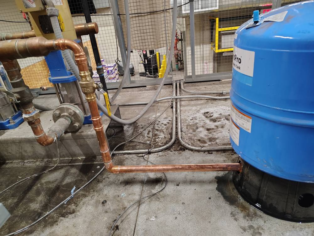 Commercial booster pump skid piped in Type L copper to a blue bladder expansion tank.