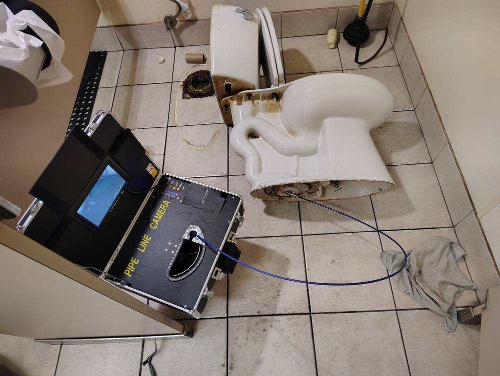 Pipe line camera monitor beside a toilet that has been pulled, with the camera line fed into the closet flange.