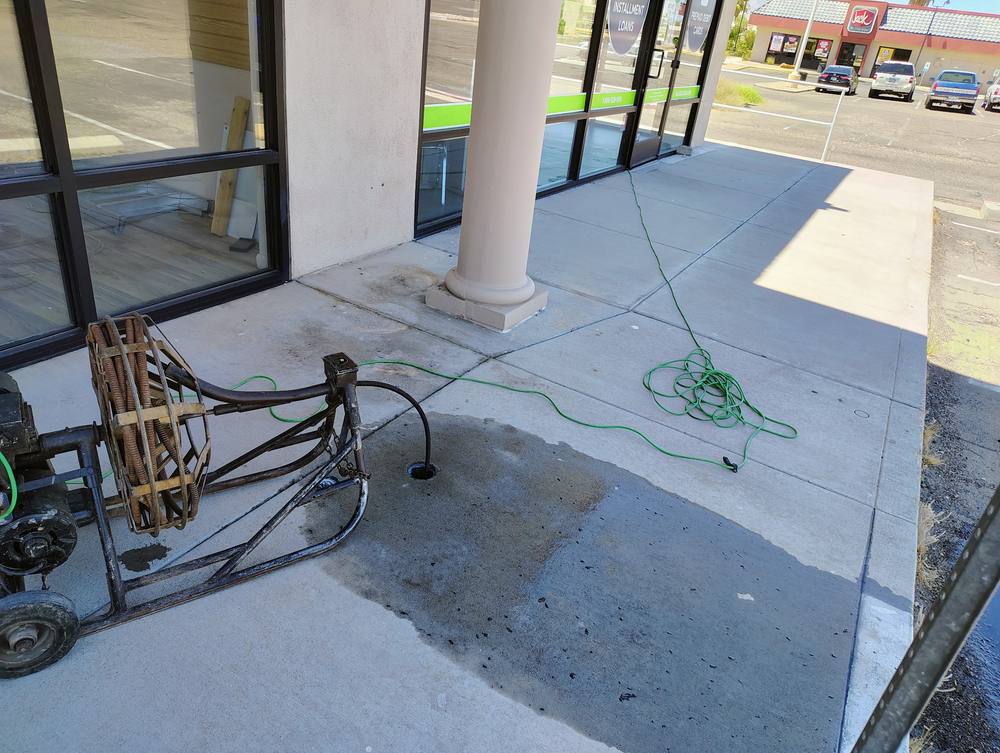 Large sectional drain machine set up at an exterior clean-out outside a commercial storefront.
